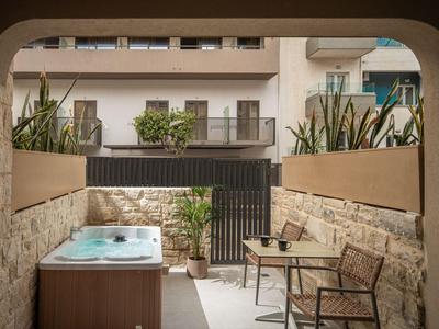 Gemütlicher Außenbereich mit Whirlpool, Tisch und Stühlen vor einem modernen Hotelgebäude.