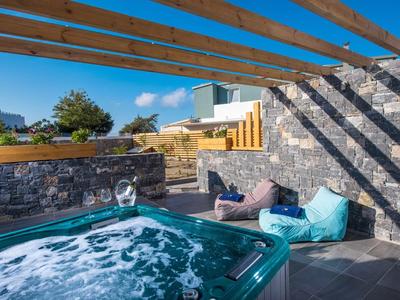 Modern outdoor hot tub under wooden beams with cushions on a terrace under clear sky.