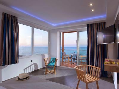 Bright hotel room with sea view, modern lighting, and balcony with chairs.