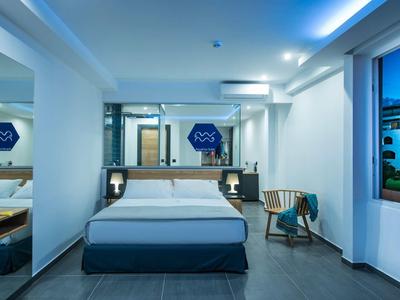 Modern hotel room with double bed, nightstands, chair, and large window with evening view.