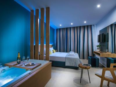 Modern hotel room with bathtub, large bed, and wooden furniture in calming colors.