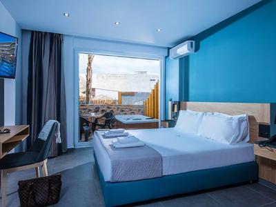 Modern hotel room with blue accent, double bed, and terrace overlooking the sea.