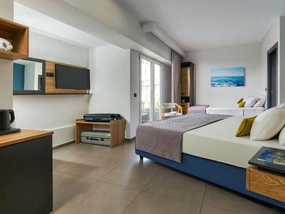 Camera d'hotel moderna con letto grande, zona salotto e balcone con vista sul mare.