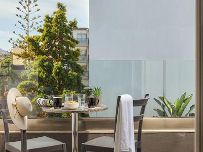 Balcone con tavolo, due sedie e vista su giardino e edifici.