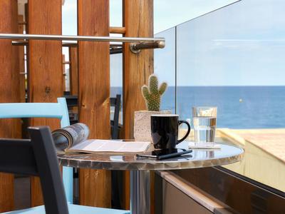 Piccolo tavolo rotondo con tazza nera e bicchiere d'acqua su balcone con vista mare.