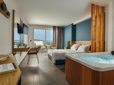 Camera d'hotel moderna con letto matrimoniale, scrivania e vasca idromassaggio vicino alla finestra con vista sul mare.