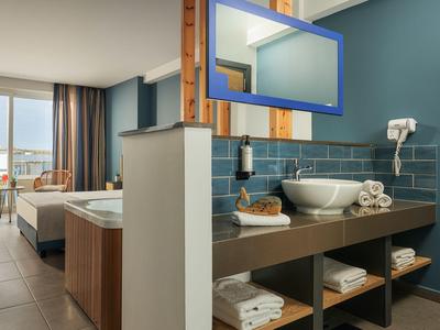 Camera d'hotel moderna con lavandino, specchio e balcone con vista sul mare.