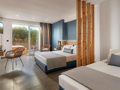 Camera d'hotel moderna con due letti, scrivania, zona soggiorno e vista sul giardino.