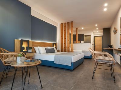 Camera d'hotel moderna con due letti matrimoniali, sedie in rattan e un piccolo tavolo.