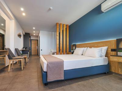 Camera d'hotel moderna con letto grande, area salotto, accenti in legno e parete blu.