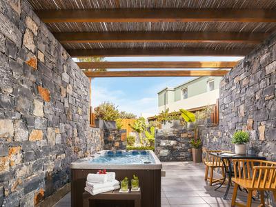 Una vasca idromassaggio esterna in un'area con pareti in pietra, soffitto di legno e zona salotto.