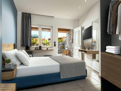 Camera d'hotel luminosa con letto matrimoniale, finestra, TV e armadio aperto con vestiti.