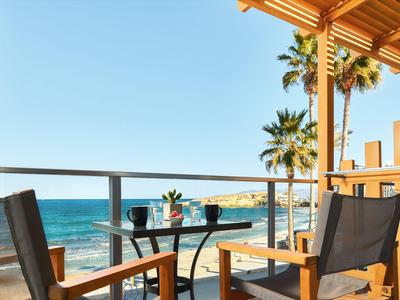 Balcone con mobili in legno e vista mare sotto un cielo limpido con palme.