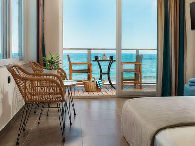 Hotelzimmer mit Balkon, Meerblick, zwei Stühlen und Tisch auf Holzboden.