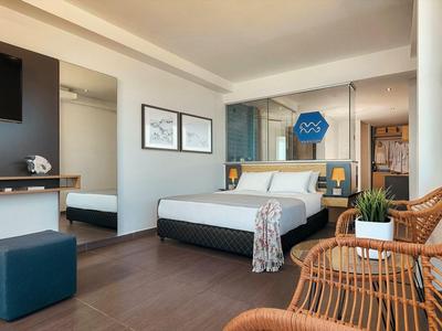 Camera d'hotel moderna con letto matrimoniale, scrivania, sedie e balcone con vista mare.