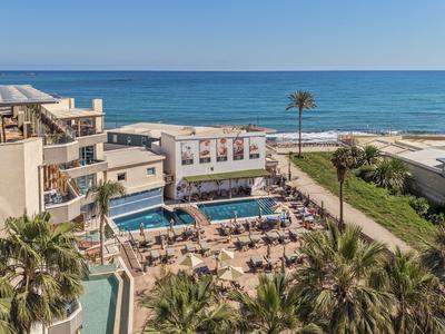 Hotel mit Pool, Liegestühlen und direktem Zugang zum Strand bei klarem Himmel.