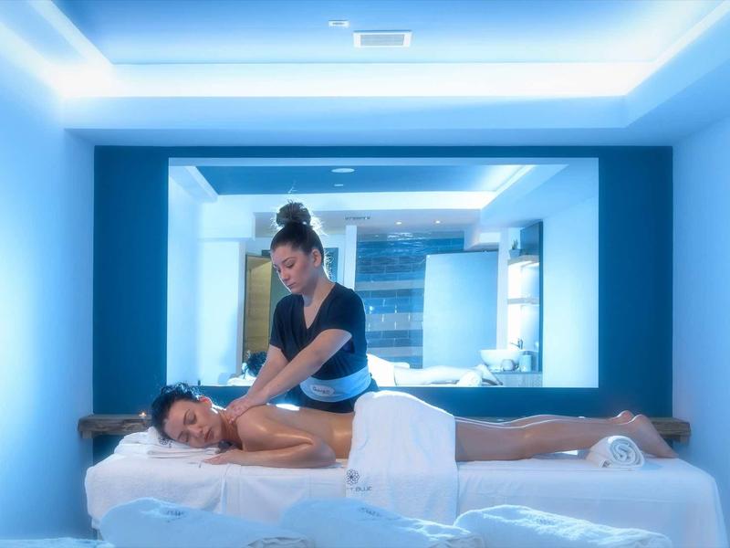 Woman receives massage on white massage table in calm, blue-lit room.