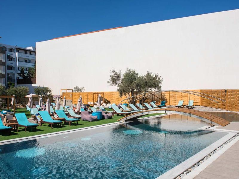 Modern outdoor pool with lounge chairs and umbrellas in front of a white hotel wall.