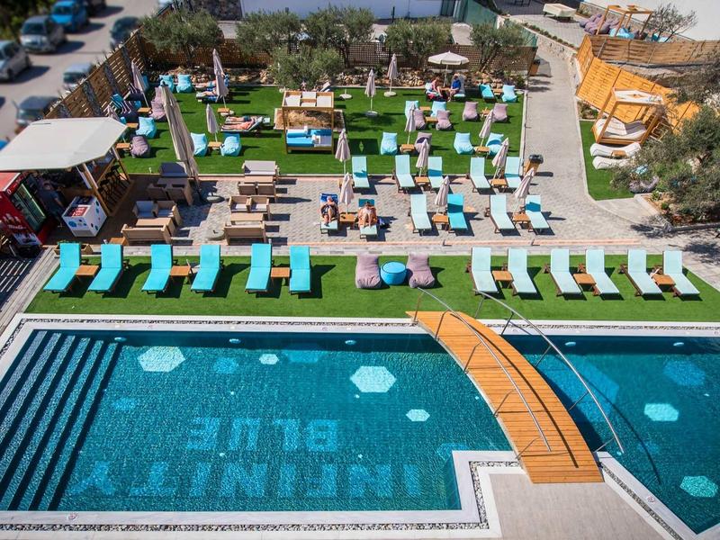 Modern outdoor pool with sun loungers and wooden arch bridge at a hotel resort.