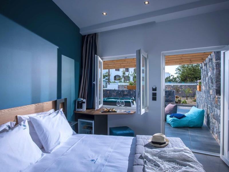 Modern hotel room with double bed and access to a terrace with seating and greenery view.