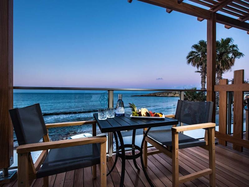 Balcony overlooking the sea, two chairs and a table with drinks at sunset.