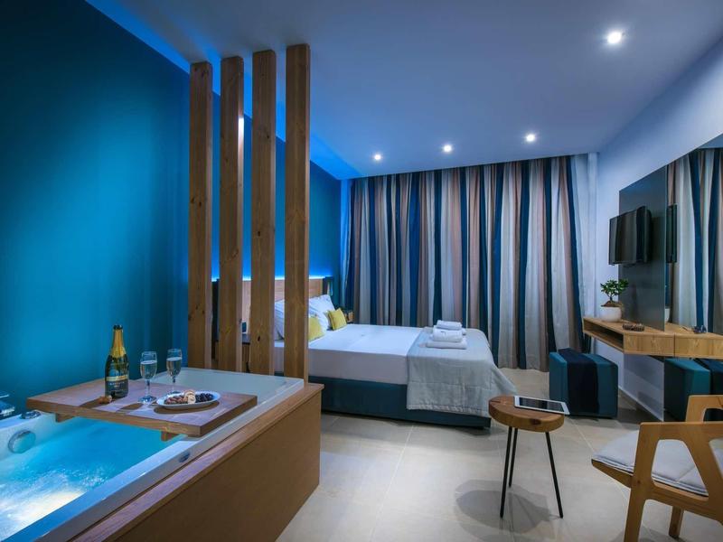 Modern hotel room with bathtub, large bed, and wooden furniture in calming colors.