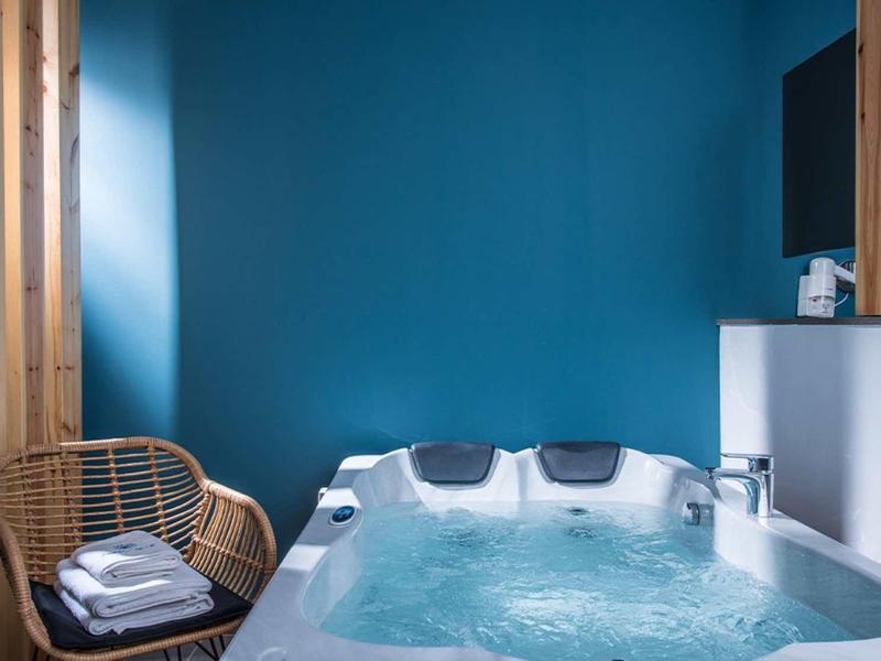 Modern whirlpool with blue wall, rattan chair, and towels nearby.