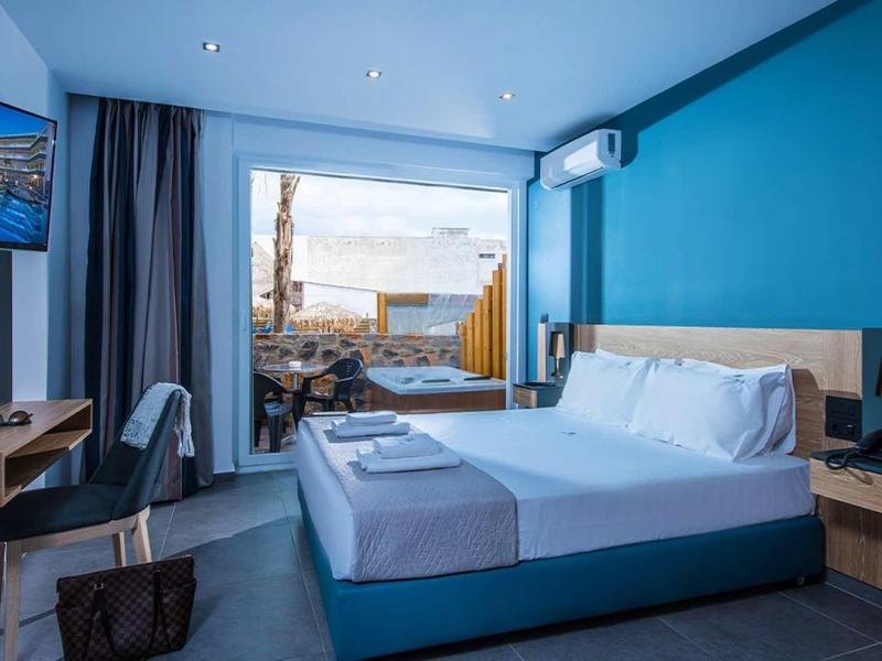 Modern hotel room with blue accent, double bed, and terrace overlooking the sea.