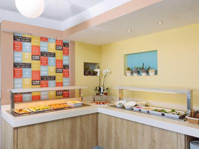 Einladender Frühstücksbereich mit Buffet, gelben Wänden und farbenfrohem Spruchposter.