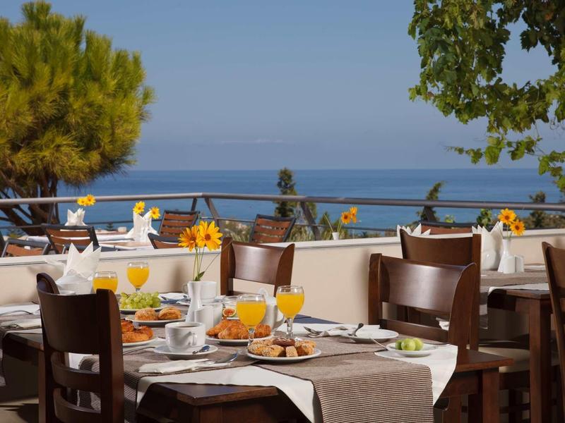Terrassenrestaurant mit gedeckten Tischen, braunen Stühlen, Blumen und Meerblick im Hintergrund.