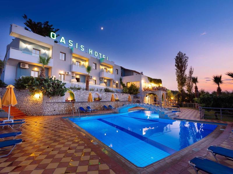 Hotel mit beleuchtetem Pool, blauer Abendhimmel, Sonnenschirme und Palmen im Hintergrund.