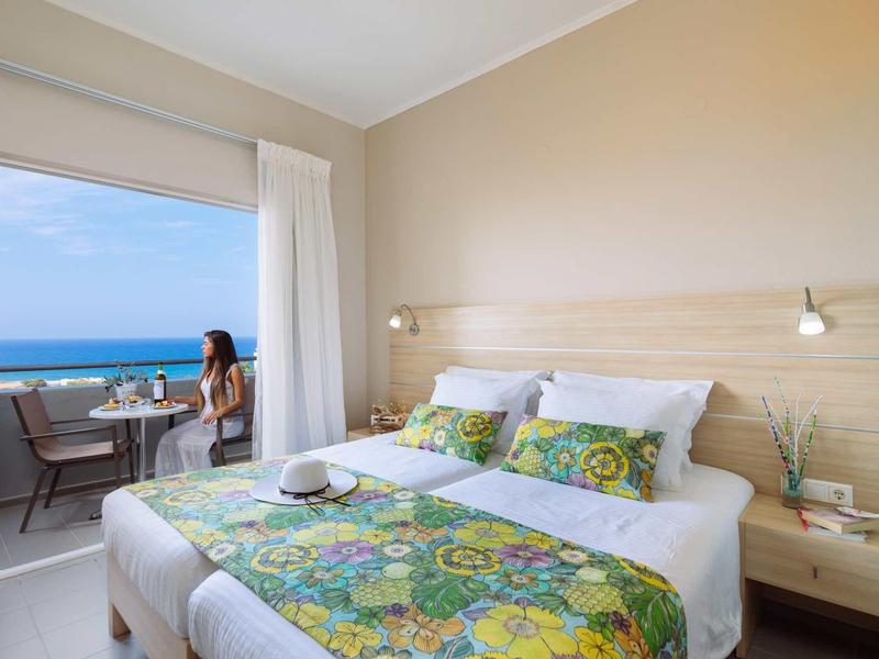 Hell eingerichtetes Doppelzimmer mit großem Bett und Balkon mit Meerblick.