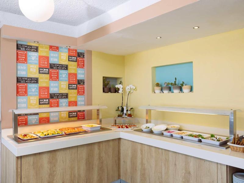 Einladender Frühstücksbereich mit Buffet, gelben Wänden und farbenfrohem Spruchposter.