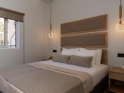 Modern eingerichtetes Hotelzimmer mit Doppelbett, hellen Wänden und hängenden Lampen neben dem Bett