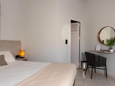 Schlafzimmer mit Doppelbett, Nachttischlampe und Schreibtisch mit Stuhl und Spiegel.