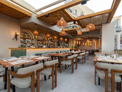 Hell eingerichtetes Hotelrestaurant mit Holztischen, Stühlen und moderner Beleuchtung unter Glasdach.