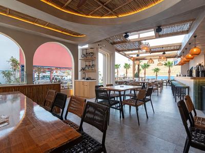 Helles Hotelrestaurant mit Holztischen, modernen Stühlen und Meerblick durch große Fenster.