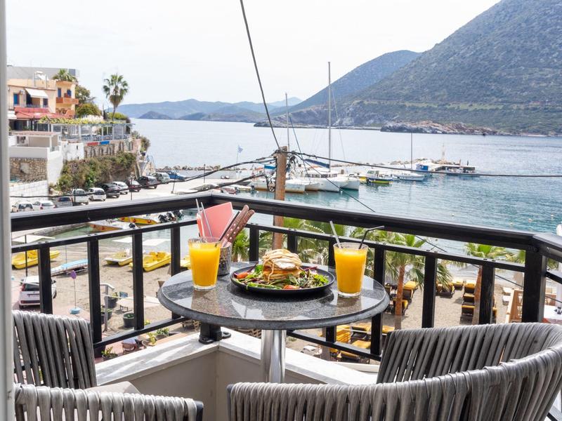 Balkon mit Tisch, zwei Sesseln, Essen und Getränken mit Blick auf das Meer und Berge.