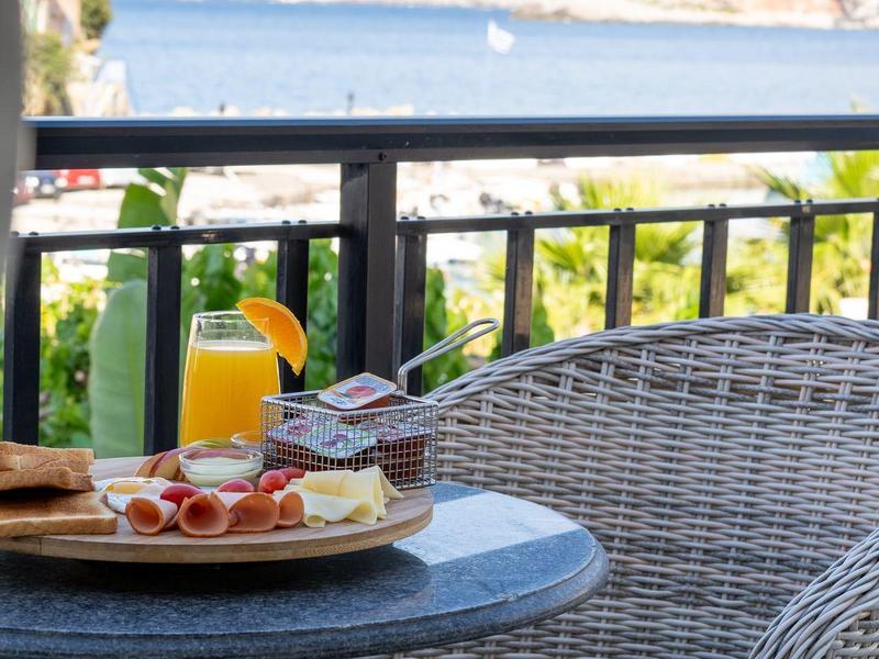 Ein Balkon mit Tisch und Stuhl, auf dem Tisch Frühstück vor Meerblick steht.