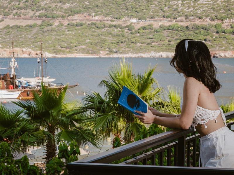 Frau am Balkon mit Blick auf Palmen und das Meer bei sonnigem Wetter.