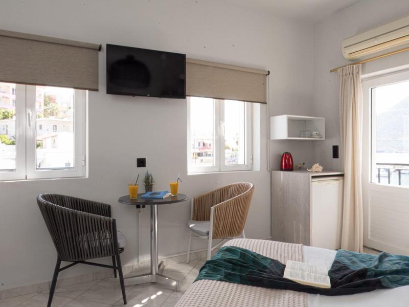 Helles Hotelzimmer mit Bett, zwei Stühlen, kleinem Tisch, Fernseher und Zugang zu Balkon.