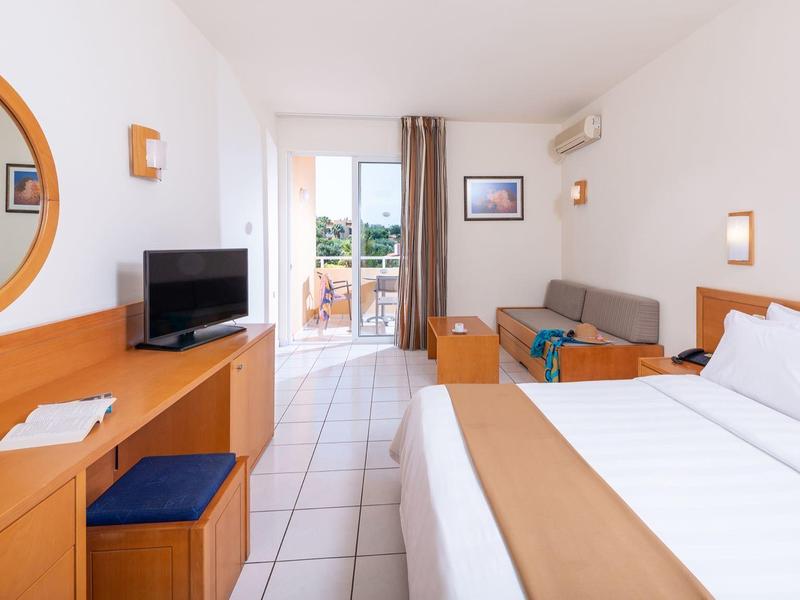 Nowoczesny pokój hotelowy z podwójnym łóżkiem, telewizorem i balkonem z widokiem na zewnątrz.