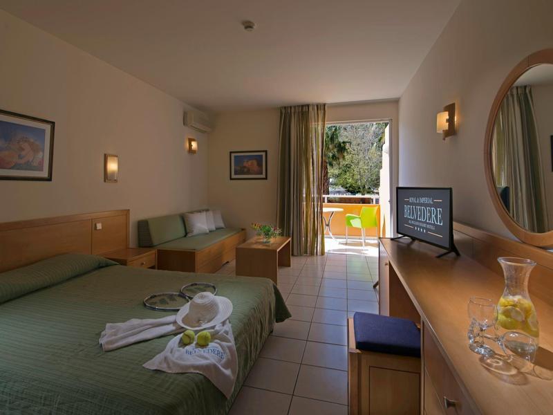 Jasny pokój hotelowy z podwójnym łóżkiem, kanapą, biurkiem i widokiem na taras z ogrodem.