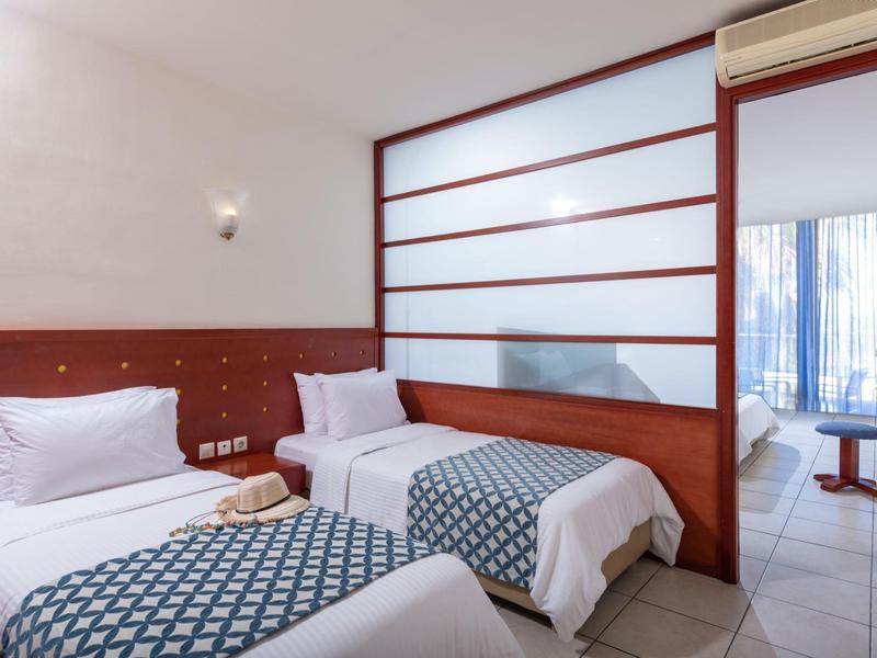 Pokój hotelowy z dwoma pojedynczymi łóżkami, drewnianymi panelami i przegrodą, widok na sąsiedni pokój.