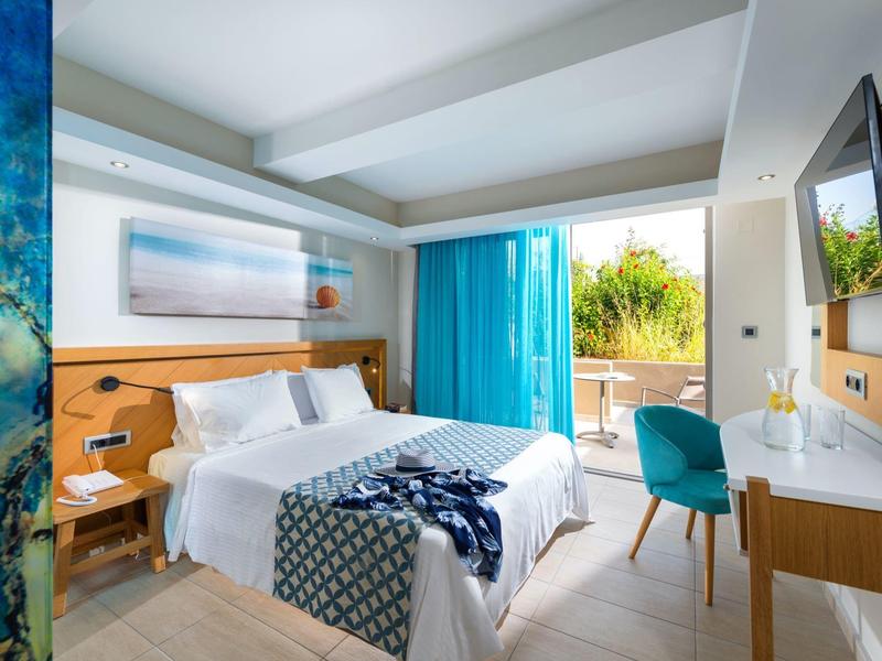 Nowoczesny pokój hotelowy z podwójnym łóżkiem, biurkiem, balkonem i niebieskimi zasłonami.