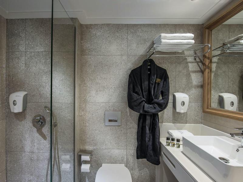 Nowoczesna łazienka z kabiną prysznicową, toaletą, czarnym szlafrokiem i dużym lustrem.