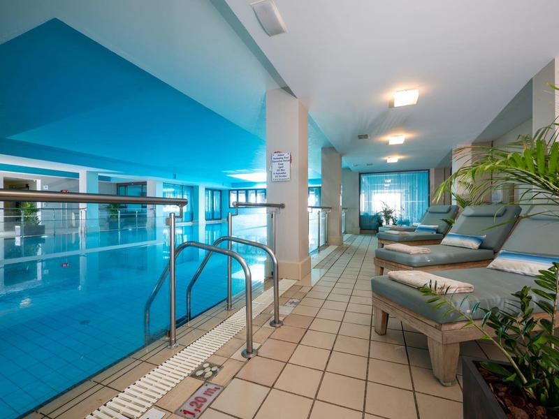 Nowoczesny kryty basen z leżakami i roślinami w części hotelowej.