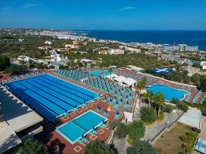 Duży basen na zewnątrz z leżakami i zielenią w hotelowym kurorcie blisko morza.