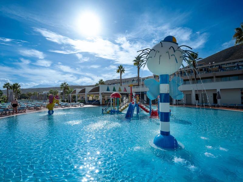 Basen na zewnątrz z placem zabaw wodnych, palmami i słońcem w hotelu