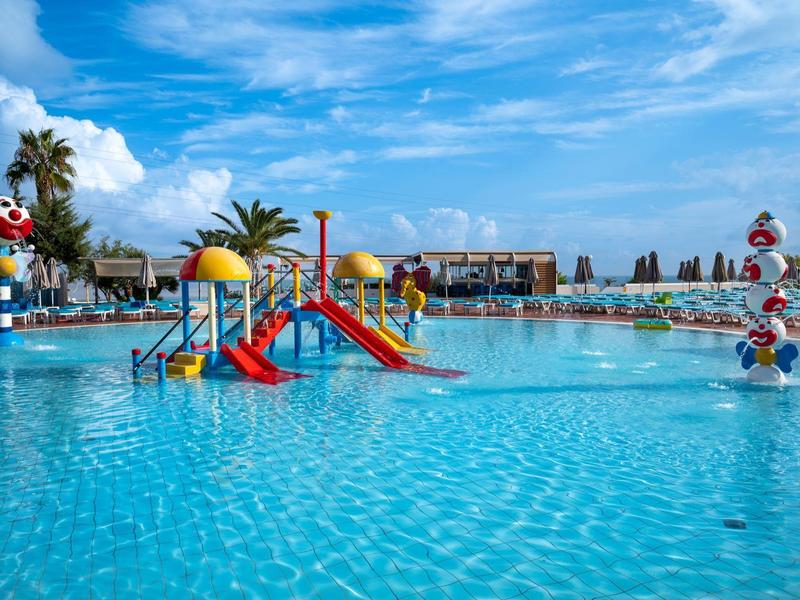 Duży basen z kolorowym placem zabaw dla dzieci i wodnymi atrakcjami pod niebieskim niebem.